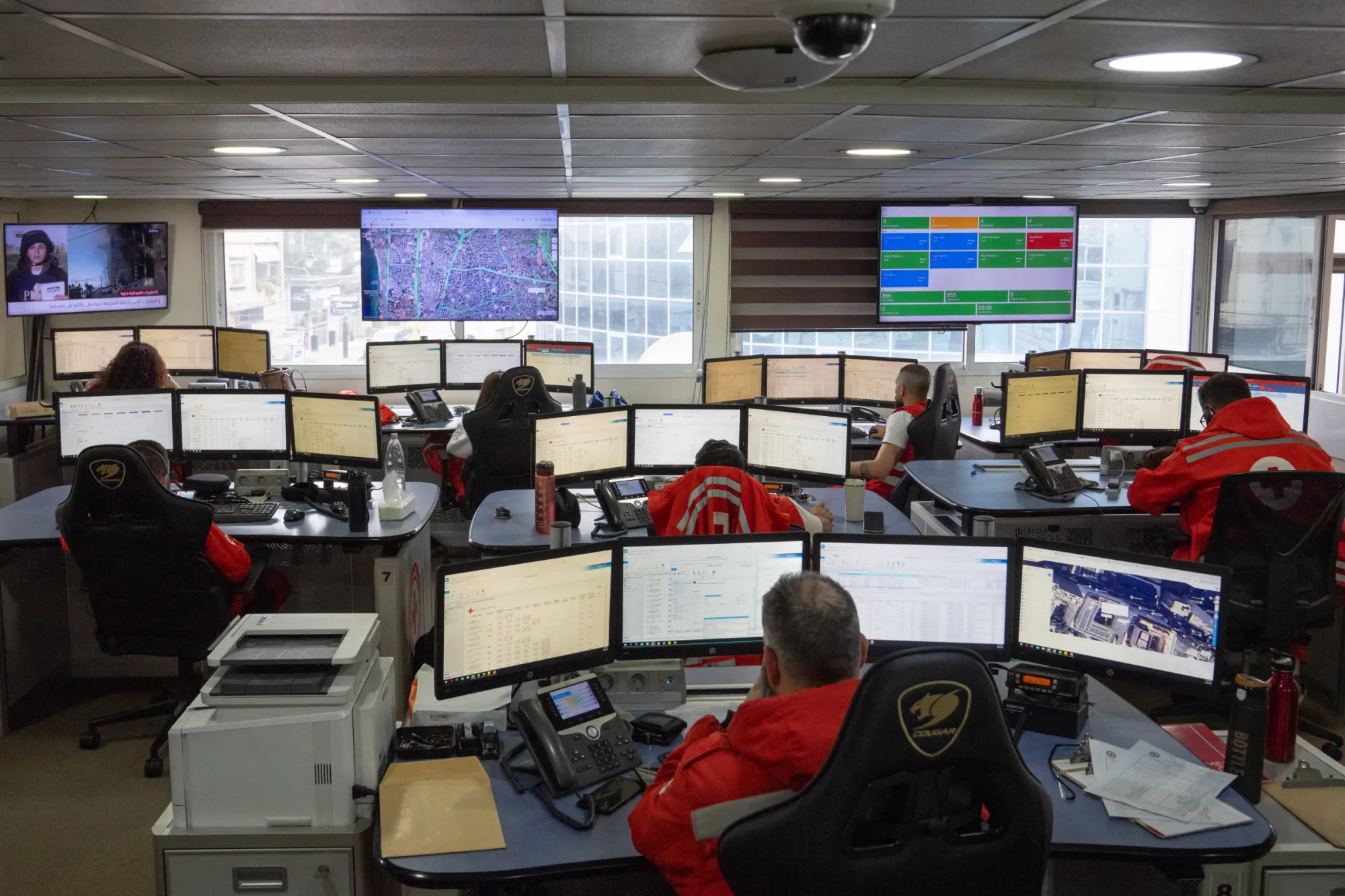 Eight people sit at desks with 3-4 monitors at the Red Cross dispatch center in southern Beirut.