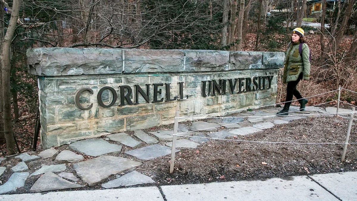 A woman walking past a Cornell University sign in Ithaca, New York