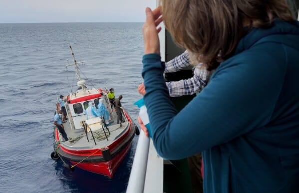 ผู้โดยสารบนเรือสำราญ MV Hondius ที่มีการระบาดของไวรัสฮันตา มองดูนักระบาดวิทยาขึ้นเรือที่เมืองไปรอา ระหว่างการเดินทางไปยังท่าเรือ Tenerife ของสเปน เมื่อวันที่ 6 พฤษภาคม 2026 (ภาพ AP)