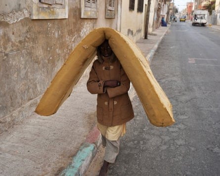 A young boy walks along a road with a foam mattress balanced on his head