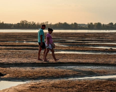 People walk on the exposed riverbed of the Danube River in Dunaszentbenedek, Hungary.