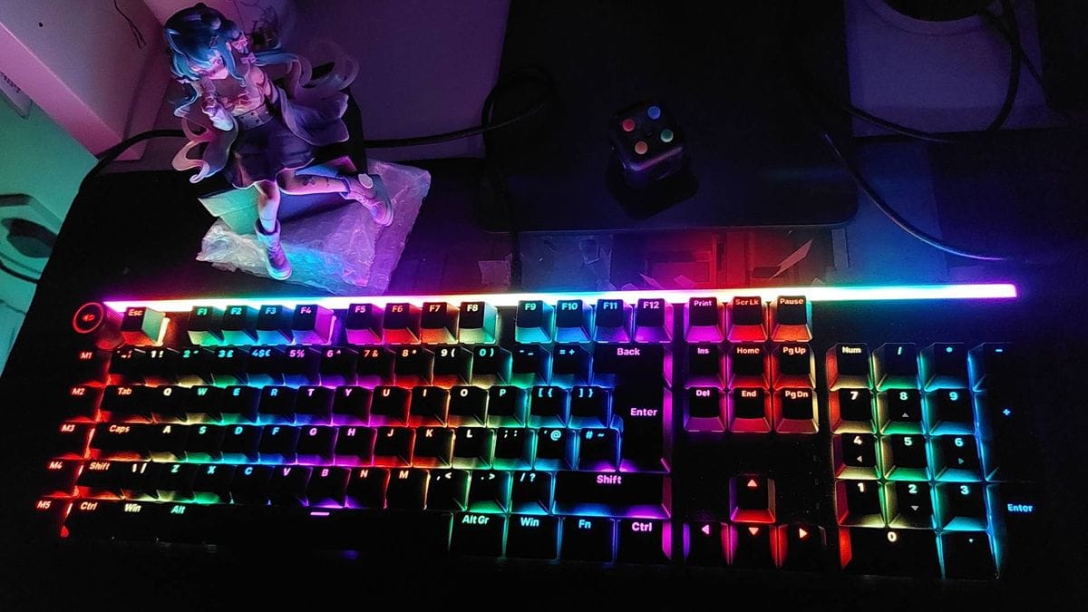 ในห้องมืด คีย์บอร์ดเมคานิคอล Light Mount ของ Be Quiet เปิดไฟ RGB ส่องสว่างฟิกเกอร์อนิเมะ Hatsune Miku และฟิดเจ็ตคิวบ์ใกล้ๆ