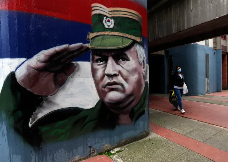 A woman wearing a face mask walks past graffiti depicting former Bosnian Serb wartime general Ratko Mladic in Belgrade, Serbia