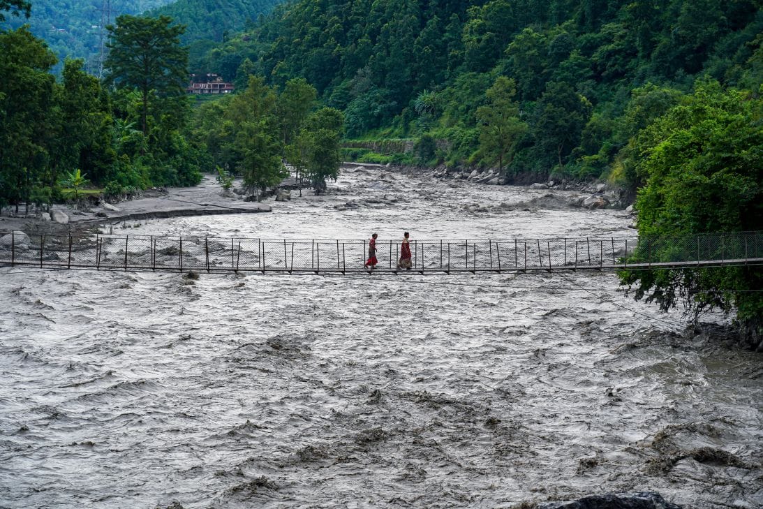 ผู้คนเดินข้ามสะพานแขวนเพื่อข้ามแม่น้ำตริศูลีที่ท่วมสูงในเมืองไบเซ เขตนูวาโกฏ ประเทศเนปาล เมื่อวันที่ 8 กรกฎาคม 2025