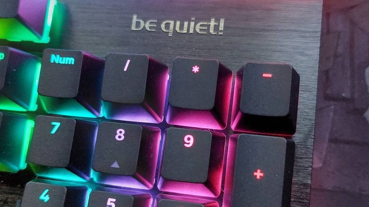 ภาพระยะใกล้ของคีย์บอร์ดเมคานิคอล Light Mount เหนือแป้นตัวเลขมีโลโก้ 'be quiet!' ตัวอักษรโลหะมันวาว เปิดไฟ RGB